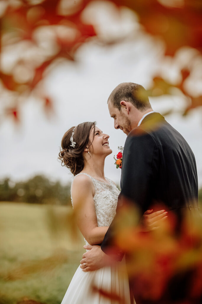 Wedding Photography: Happy male and female couple embracing through autumn leaves at their wedding